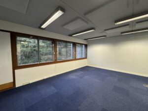 Empty office space with blue carpet, white walls, and large windows at De Ruijterkade.